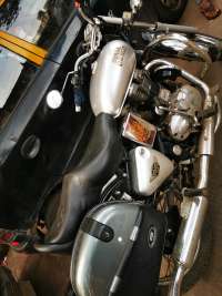 Silver Royal Enfield Bullet Classic 350 motorcycle with black seat and gray storage pannier, parked next to a black taxi.