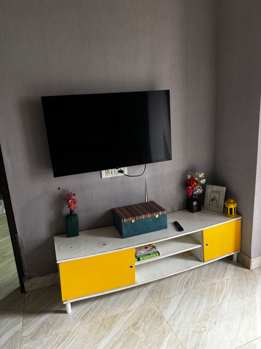 Yellow and white tv unit with a television mounted above, next to a doorway on a tiled floor.