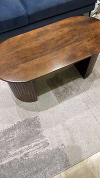 Oval imported coffee table with dark brown wood top and unique fluted base, near a blue sofa on a grey rug.