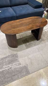 Oval dark wood coffee table with slatted base sits next to a blue sofa on a patterned rug.