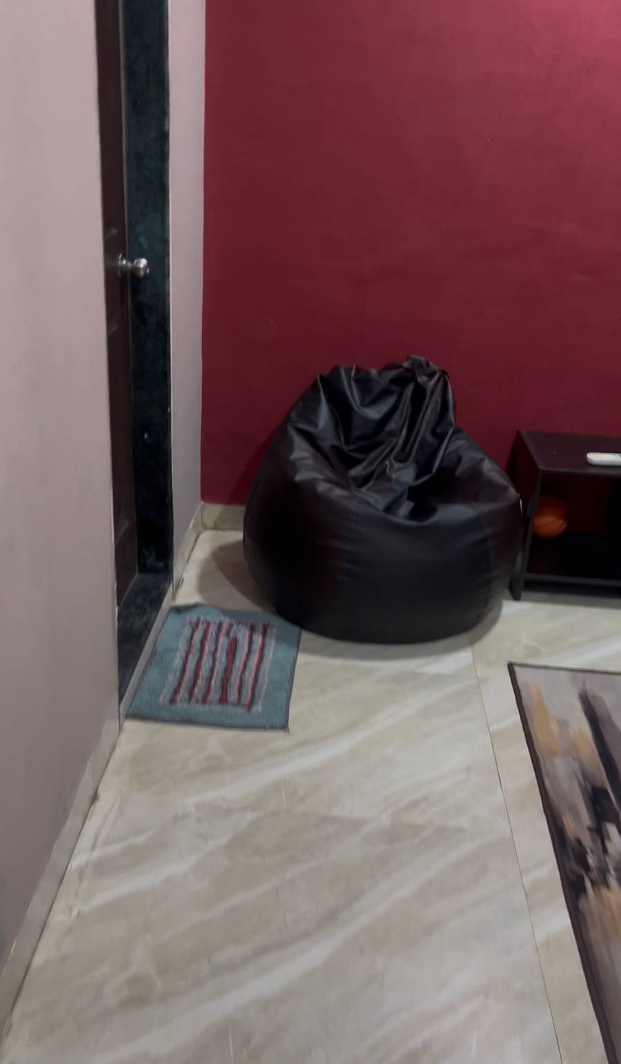 Black bean bag chair on a light tiled floor next to a dark red wall and small rug.